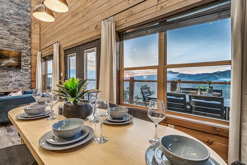Dining table set with plates and glasses beside mountain-view windows