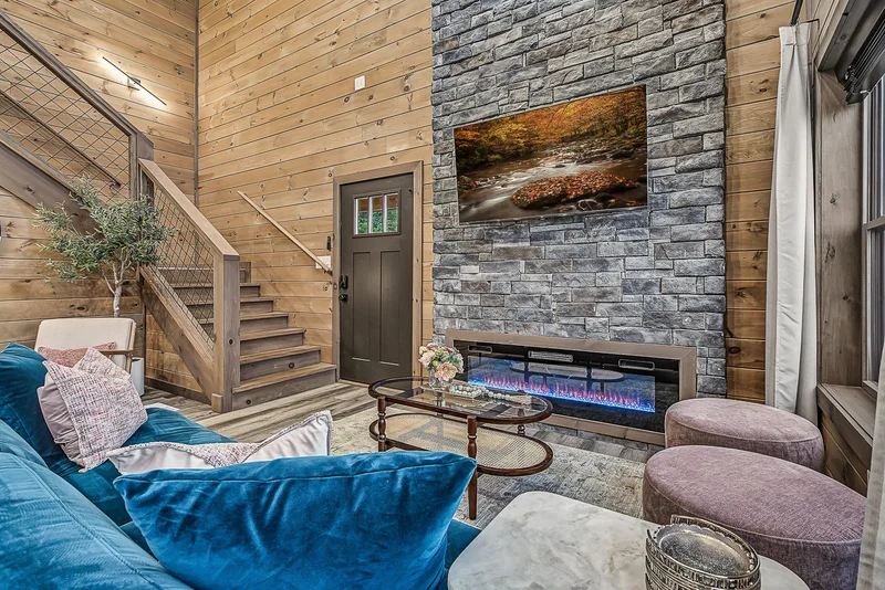 Living room with blue sofa, stone fireplace, and staircase
