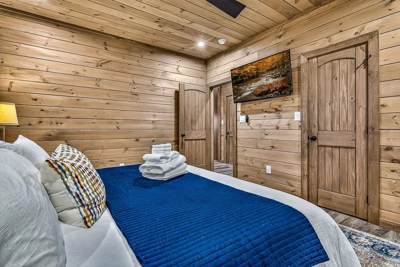 Made bed with blue coverlet, wood-paneled walls, and television