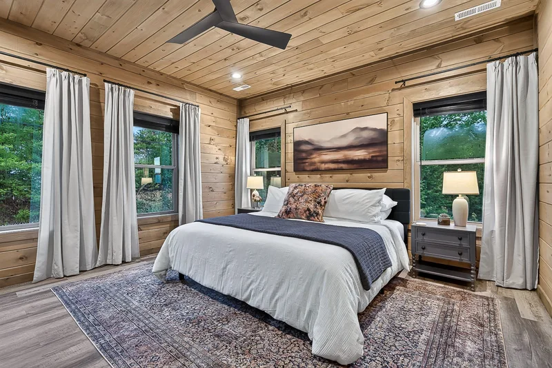 Bedroom with white bedding, dark coverlet, and landscape artwork