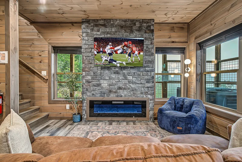 Television showing a football game above a fireplace with sofa seating