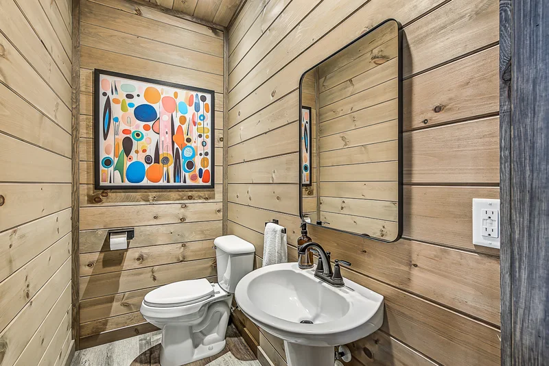 Small bathroom with toilet, pedestal sink, and colorful artwork