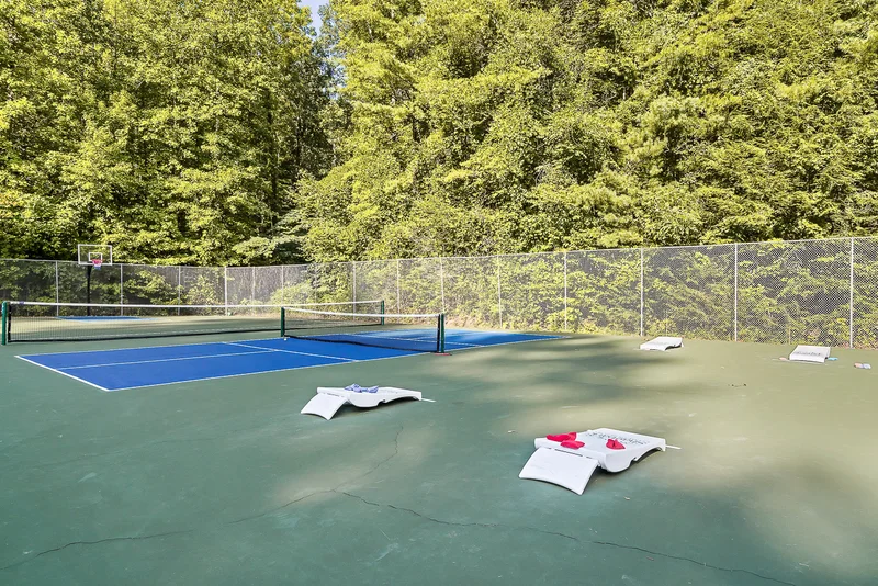 Pickleball court with cornhole boards beside a wooded fence line